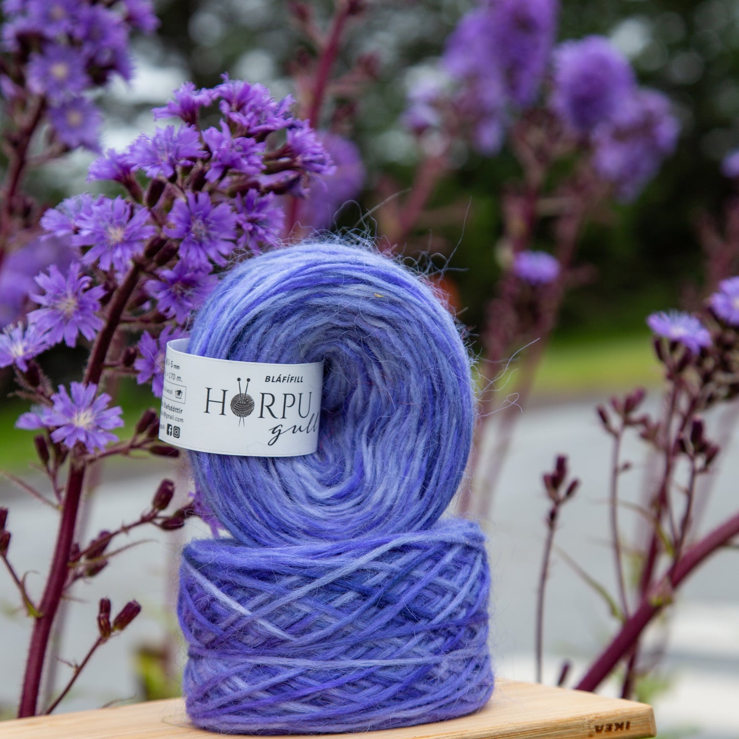 Hand-dyed Icelandic lopi yarn inspired by alpine blue sow thistle shown with matching purple flowers
