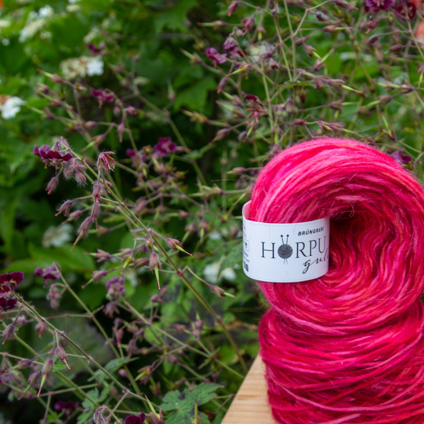 Hand-dyed Icelandic lopi yarn in vibrant pink tones displayed outdoors among flowering plants