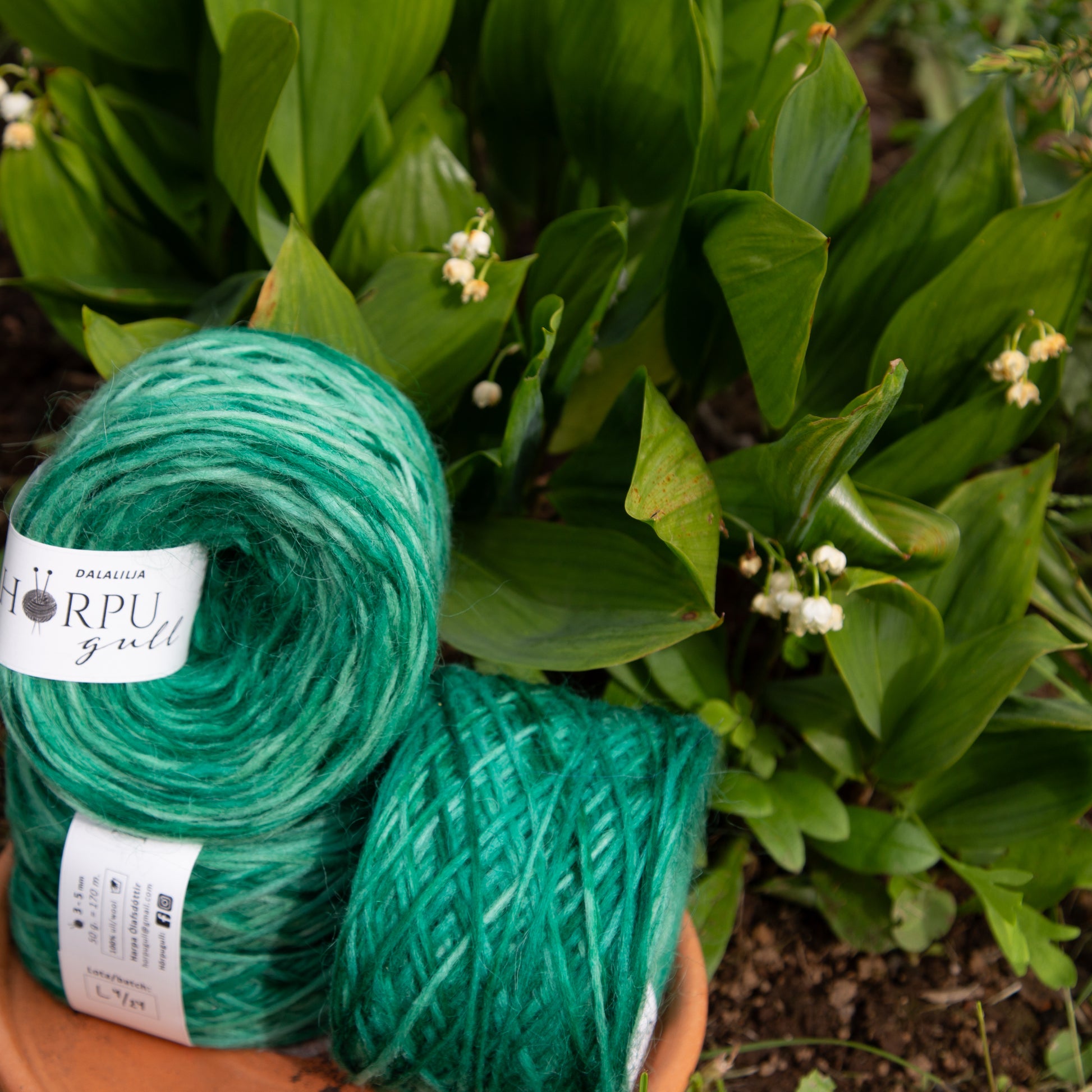 Hand-dyed green lopi yarn placed among lily of the valley plants in a natural garden setting